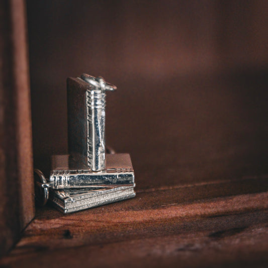 Metallic book-shaped charm on a wooden surface with a dark background