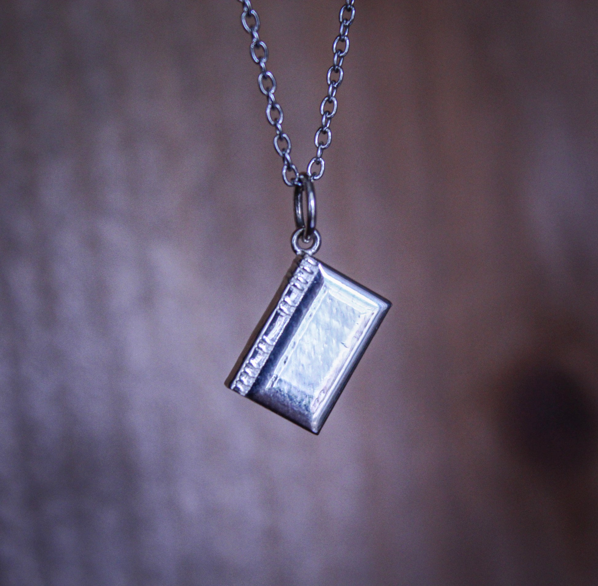 Silver book-shaped pendant on a chain against a blurred background